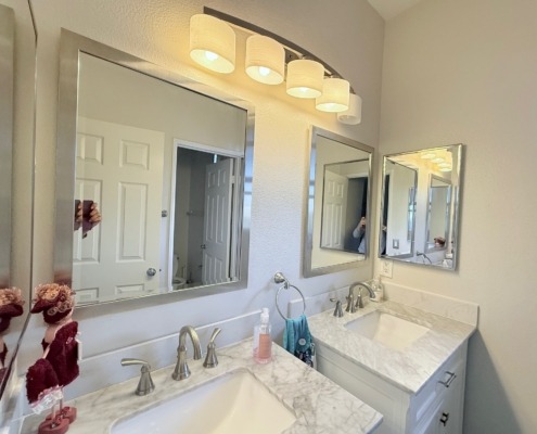 Double sink bathroom vanity with marble countertops, chrome fixtures, two mirrors, overhead lighting, and a closed door reflected in the mirrors.